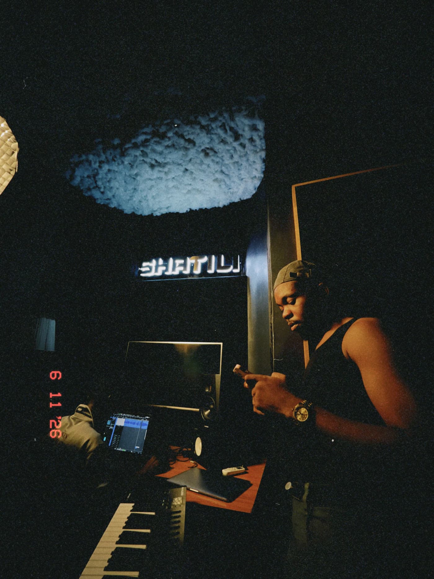 Late night in the SHATILI studio: an artist checks a phone beside the desk and keyboard.
